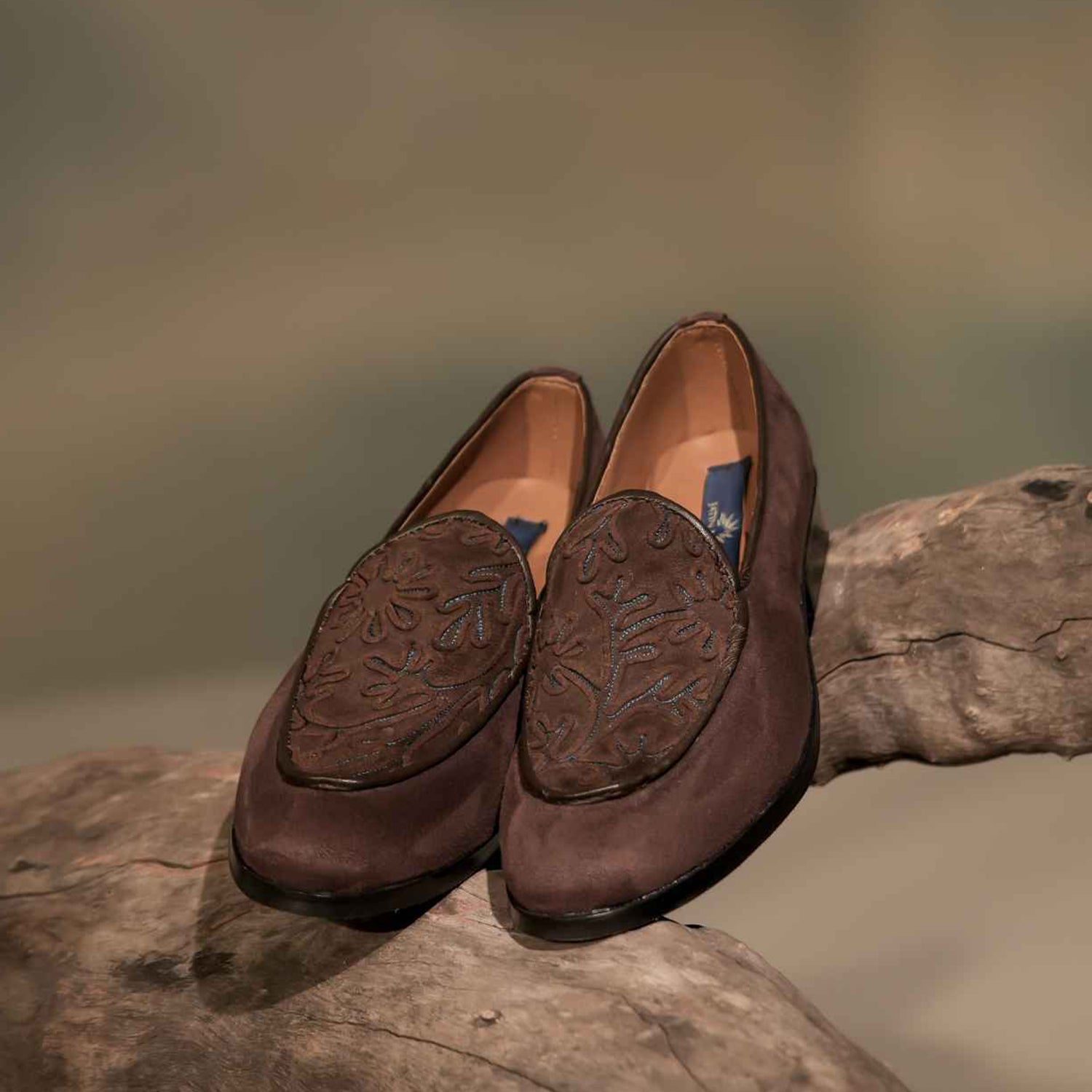 Pair of brown leather loafers with embossed floral pattern placed on a wooden surface.