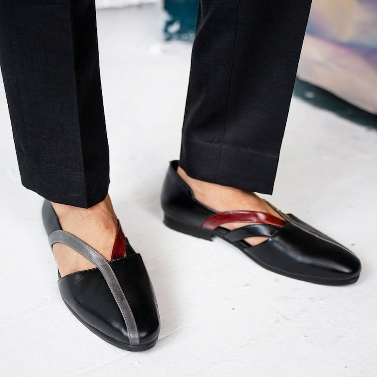 Black leather men’s loafers with cut-out sides and cross-strap detail worn with burgundy trousers, showcasing a modern and stylish slip-on shoe design