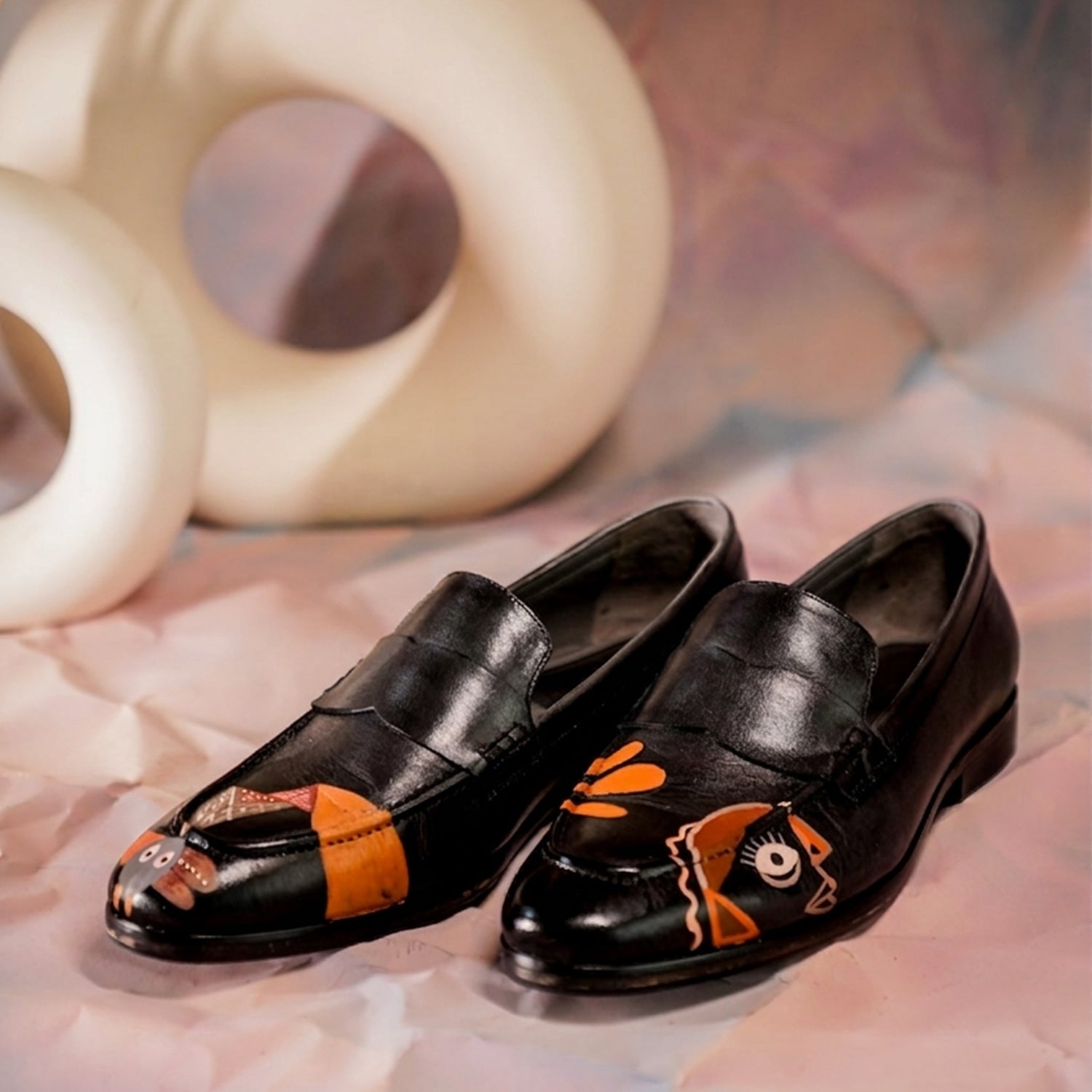 A pair of premium black leather penny loafers with a glossy finish, featuring unique hand-painted abstract artwork on the front. The design includes bold orange accents and artistic graphic elements that create a striking contrast against the black leather. The shoes have a classic slip-on style, detailed stitching, a rounded toe, and a durable sole. Ideal for both formal and smart-casual wear, these loafers combine elegance with modern artistic expression, making them perfect for men seeking stylish and di