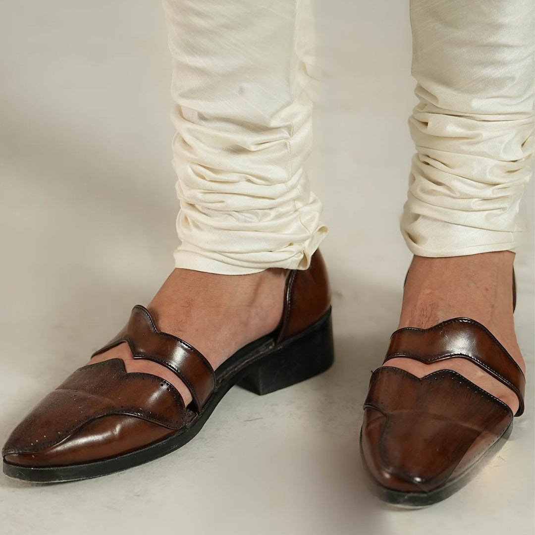 Pair of polished brown leather slip-on dress shoes with cut-out side panels and perforated detailing, featuring a sleek pointed toe and modern handcrafted design.