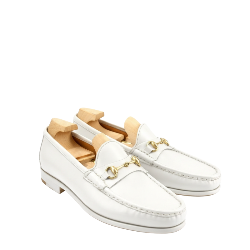 White leather horsebit loafers with gold metal detail and slip-on design on a clean background.