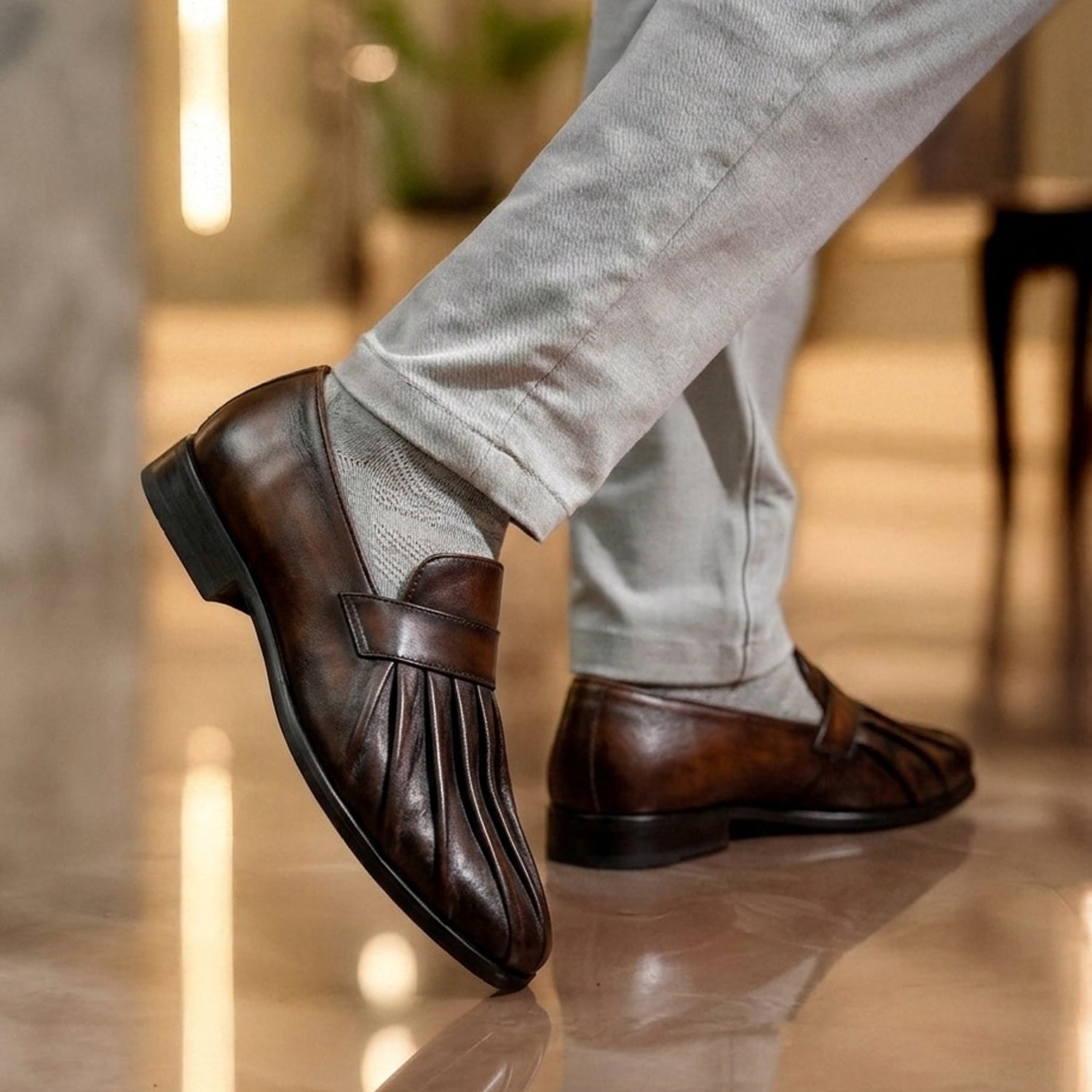 Two-tone leather slip-on loafers with black upper and brown pleated toe detail, displayed on a pedestal against a neutral background.