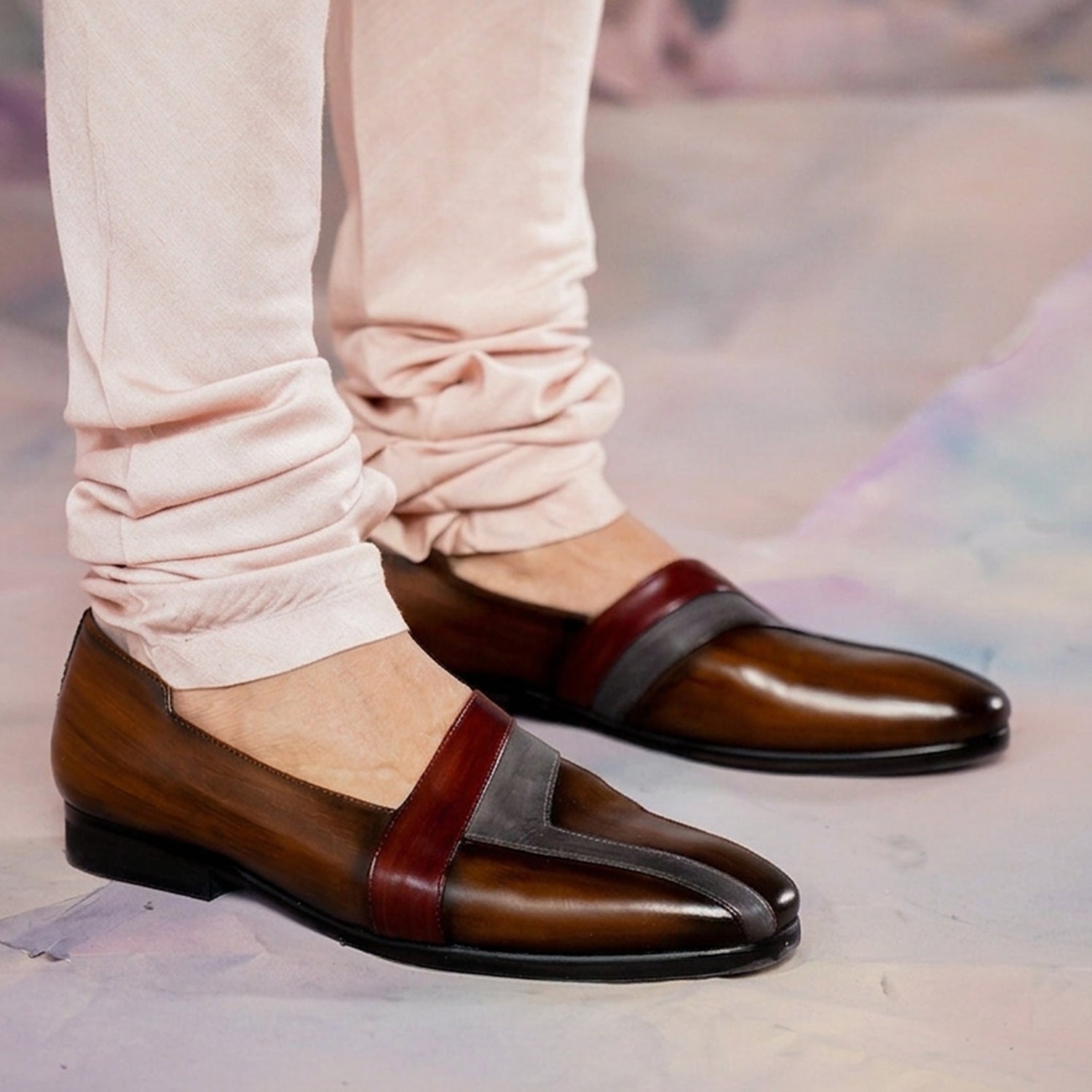 Men’s brown leather slip-on loafers with burgundy and grey accents worn with light trousers