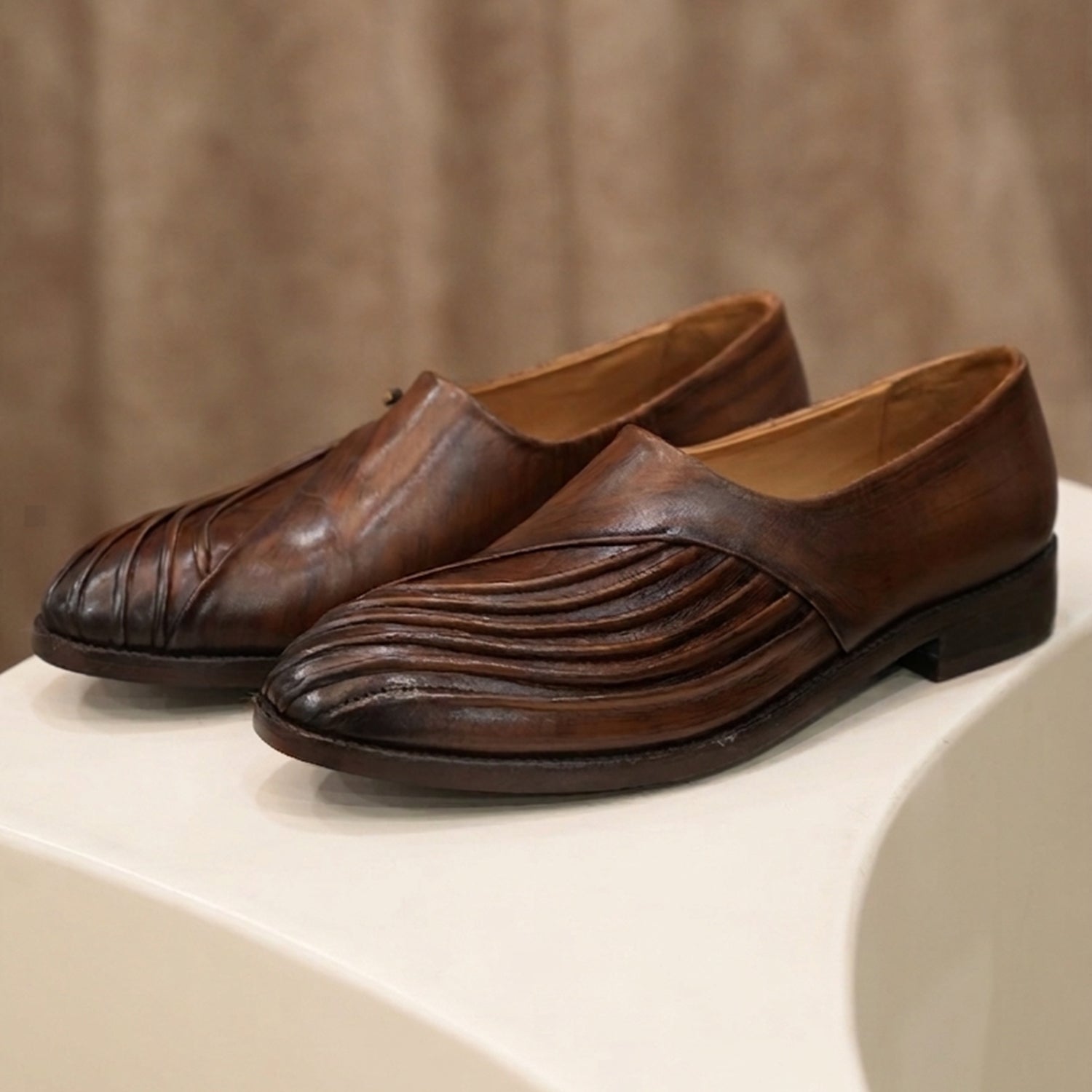 Pair of brown leather slip-on shoes with a distinctive pleated textured design on the front, featuring a polished finish and modern handcrafted style displayed on a neutral surface.