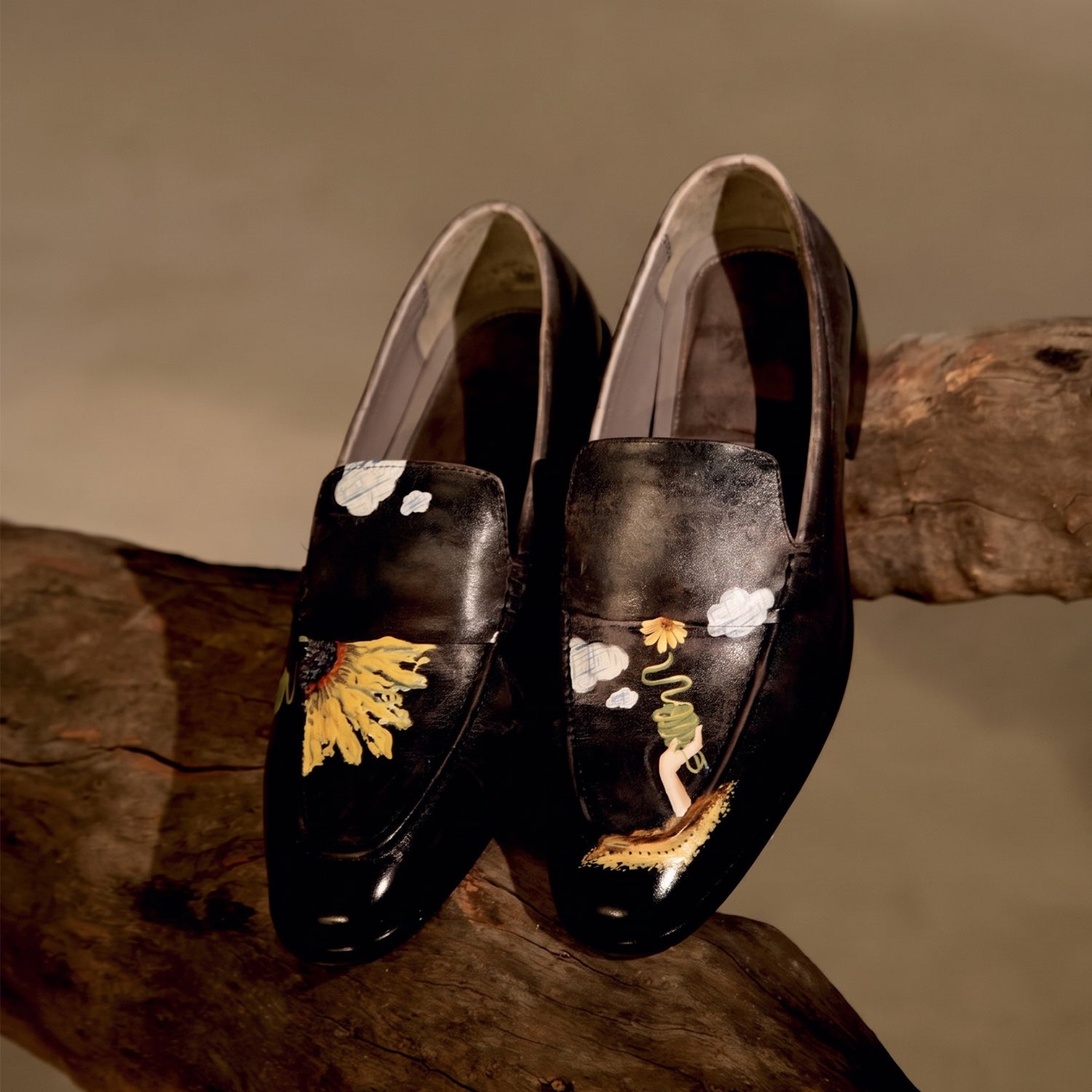 Pair of black glossy leather loafers for men with hand-painted floral and abstract artwork, square toe design, and slip-on style displayed on a rustic wooden surface.