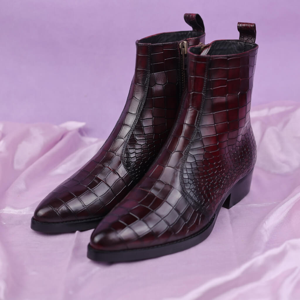 A pair of Rogue Vino cowboy boots featuring a rich, wine-colored upper crafted from crocodile skin print leather. The boots are finished with an Italian leather sole for durability and a refined look, with a handmade, eco-friendly color application by Mille Dollari, blending classic Western style with modern luxury.

