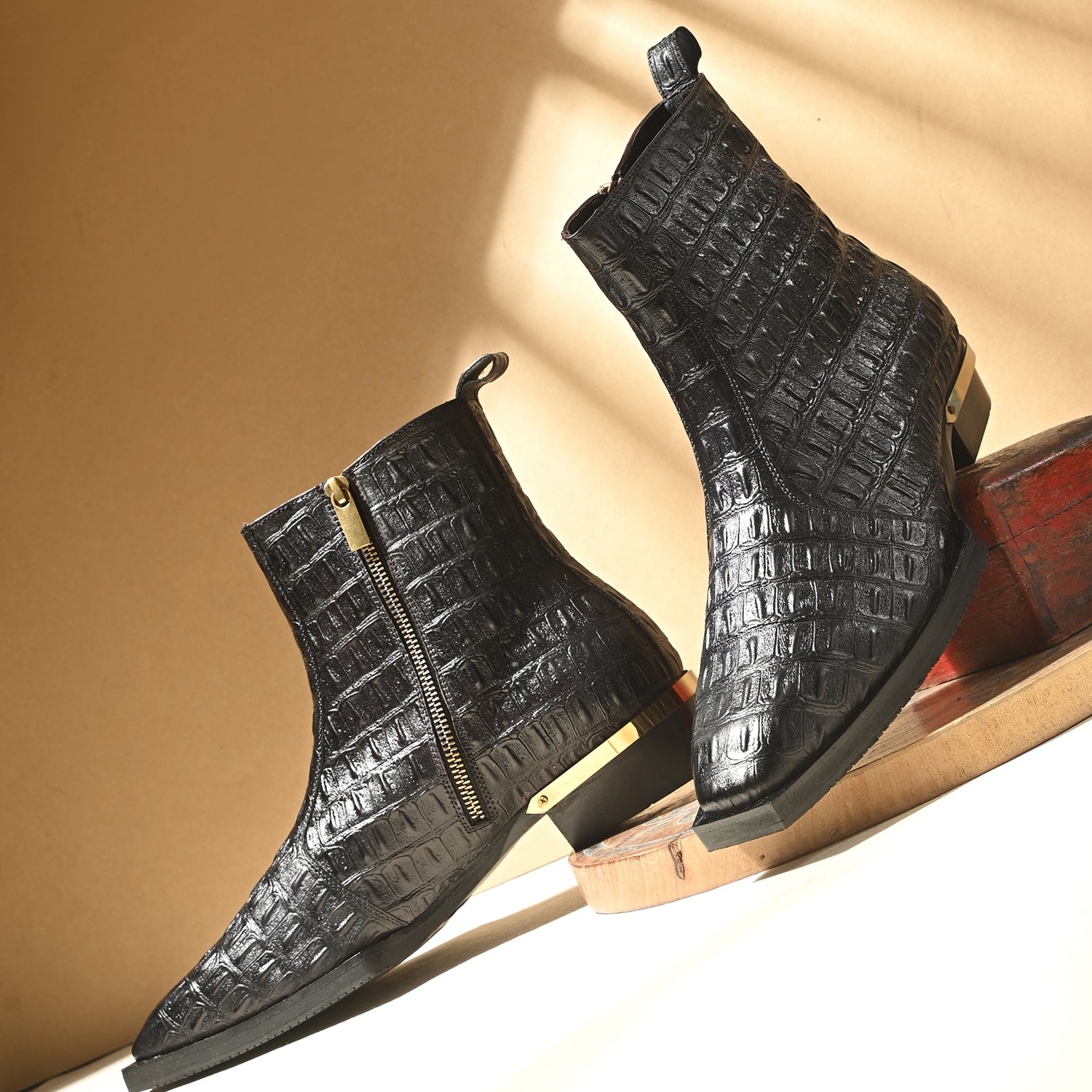 Black exotic-textured leather men’s ankle boots with gold zipper and metal heel accent.