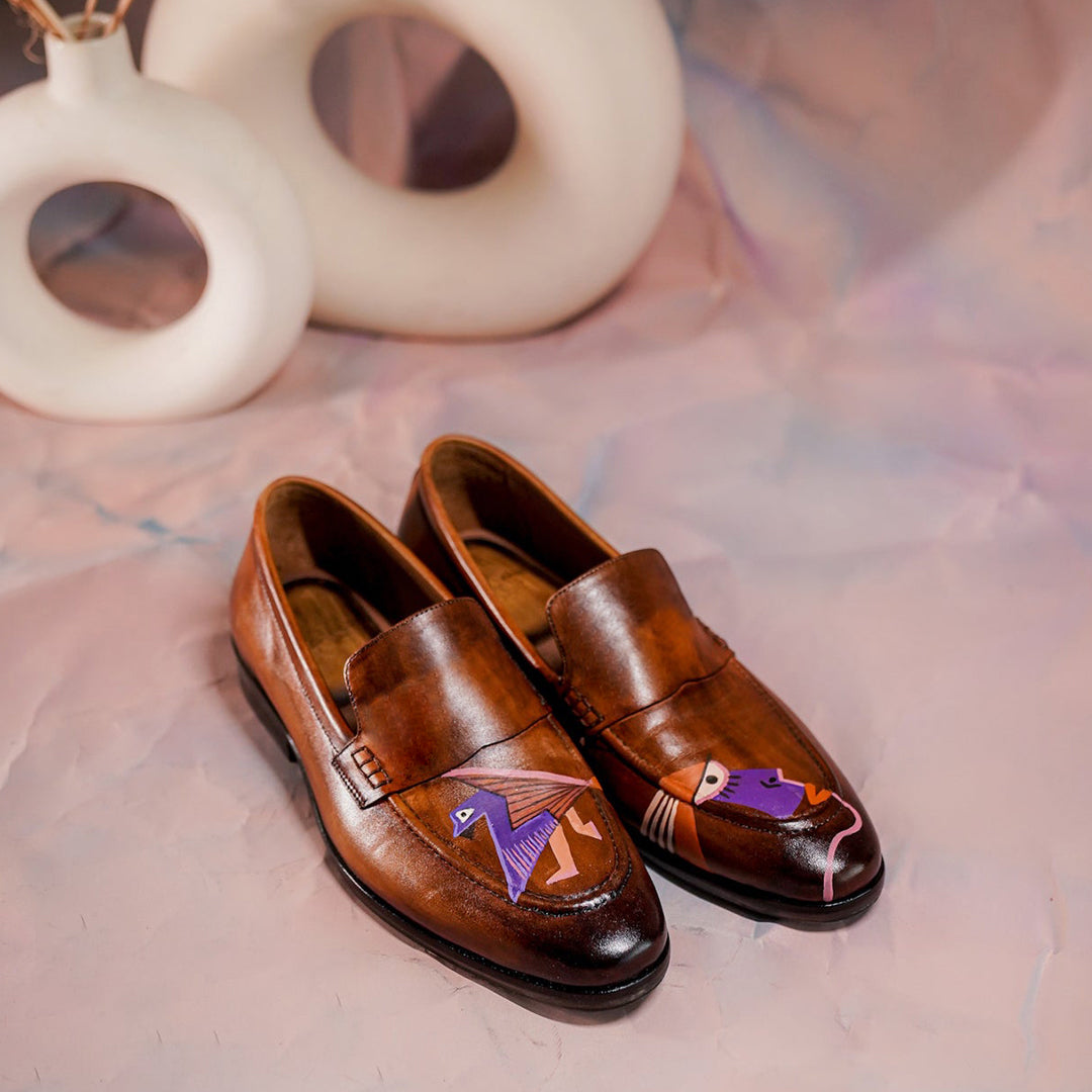 A pair of premium brown leather penny loafers featuring a glossy finish and unique hand-painted bird artwork on the front. The shoes are designed with a classic slip-on style, showcasing fine stitching, a rounded toe, and a durable black sole. The artistic bird design in vibrant colors adds a creative and eye-catching element to the otherwise traditional footwear. Ideal for formal and smart-casual wear, these loafers combine elegance with individuality, making them perfect for men who appreciate stylish and